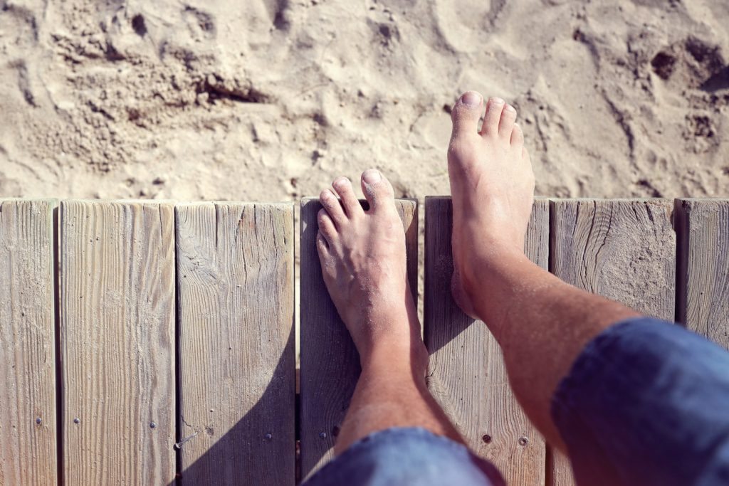 Man barefoot stepping off boardwalk onto the beach sand