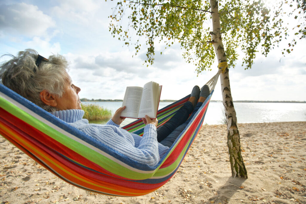 happy elderly woman enjoying in hammock at the beach, sunny autumn day